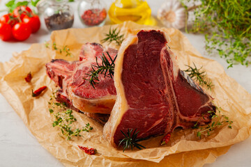 Raw t bone steak, served on paper. Herbs, stone background.