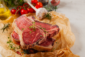 Raw t bone steak, served on paper. Herbs, stone background.