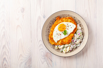 Viennese pork schnitzel with a fried egg. Served on potato salad. Natural wooden planks in the background.