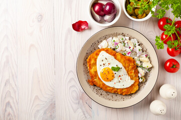 Viennese pork schnitzel with a fried egg. Served on potato salad. Natural wooden planks in the background.