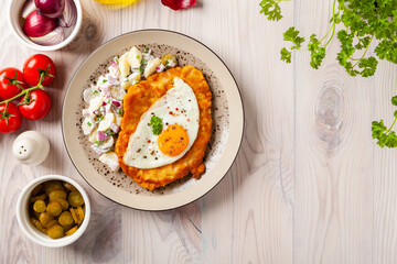 Viennese pork schnitzel with a fried egg. Served on potato salad. Natural wooden planks in the background.