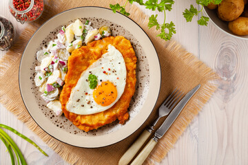 Viennese pork schnitzel with a fried egg. Served on potato salad. Natural wooden planks in the background.