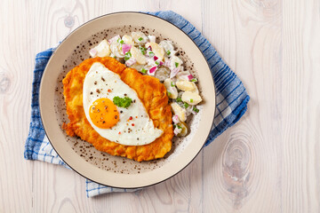 Viennese pork schnitzel with a fried egg. Served on potato salad. Natural wooden planks in the background.