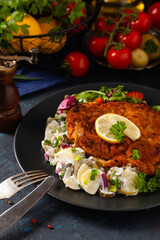 Classic, traditional Viennese sirloin schnitzel. Served on potato salad. Breaded. Dark background.
