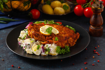 Classic, traditional Viennese sirloin schnitzel. Served on potato salad. Breaded. Dark background.