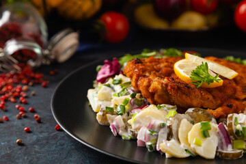 Classic, traditional Viennese sirloin schnitzel. Served on potato salad. Breaded. Dark background.