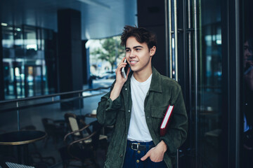 Smiling man with book calling on mobile phone