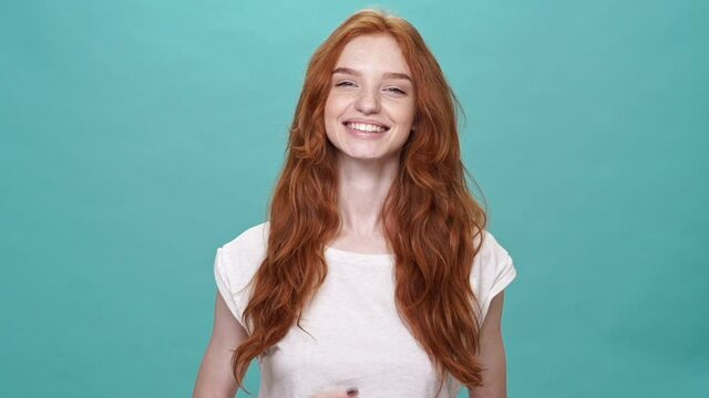 Smiling ginger woman in t-shirt sends air kiss at the camera over turquoise background