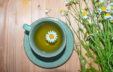 Chamomile tea, field chamomile on a wooden background. Cup of chamomile tea close up top view.