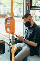 Young man wearing protective mask and using a smartphone while riding a bus