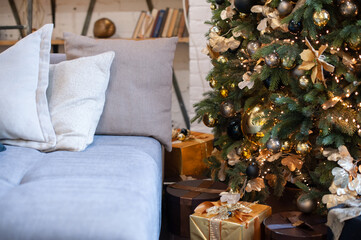 The Christmas tree is tall, decorated with golden balls and garlands, next to the sofa in the living room. Christmas tree in the interior.