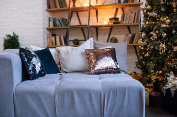 Several shiny and beige decorative pillows on a cozy gray sofa, interior.