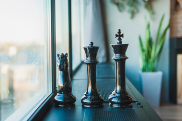 Chess pieces, black knight, king and queen, large pieces stand on a black windowsill near the window in the room.