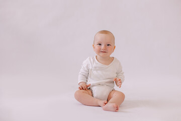 cute little kid in a white bodysuit sits on a white background. Copyspace. place for text. 8 months old boy smiling. looking at the camera. adorable child