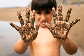 Child with naughty face and dirty hands made of sand plays on the beach.
Conceptual of lifestyle