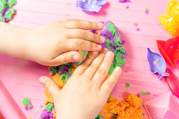 The child sculpts figures from multi-colored kinetic sand, developing fine motor skills of hands
