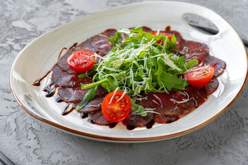 Beef carpaccio with arugula and parmesan on gray surface