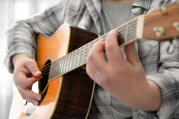 Fototapeta na wymiar A man in a plaid cowboy shirt plays country music on a western dreadnought guitar.