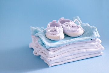 Clothes and shoes for a newborn in blue and white. Things for the little ones on a blue background. The concept of the birth of a new life and parenthood. Close-up selective focus
