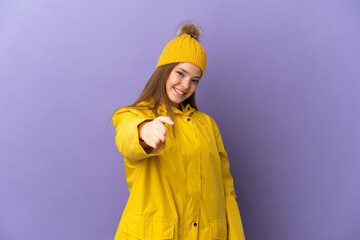 Teenager girl wearing a rainproof coat over isolated purple background shaking hands for closing a good deal