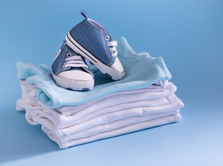 Clothes and shoes for a newborn in blue and white. Things for the little ones on a blue background. The concept of the birth of a new life and parenthood. Close-up selective focus