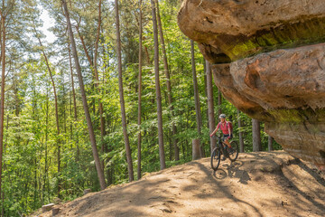 nice and active senior woman riding her electric mountain bike with full concentration on a rocks trail in the Pfaelzerwald forest near the city of Pirmasens in Rheinland-Pfalz, Germany
