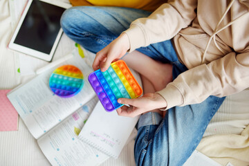 Teenage girl playing with rainbow pop-it fidget toy while studying at home. Teen kid with trendy stress and anxiety relief fidgeting game. - obrazy, fototapety, plakaty