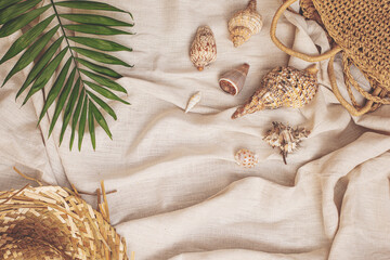 Summer background: straw hat, bag with sea shells, palm leaf on textile linen background