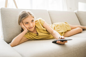 Young girl child sitting on the couch using a remote control