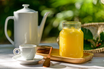 Ghee butter in glass jar on breakfast table with white teapot and cup.