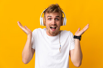 Young handsome blonde man isolated on yellow background surprised and listening music