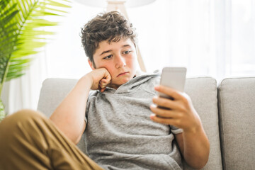 Pre-teen sit on the couch using smartphone and look sad and boring