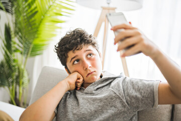 Pre-teen sit on the couch using smartphone and look sad and boring