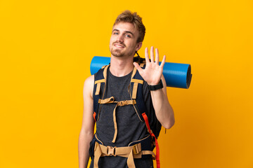Young mountaineer man with a big backpack isolated on yellow background counting five with fingers