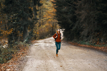 Obraz premium energetic woman running along the road with backpack in autumn forest