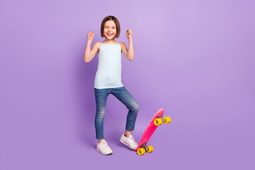 Full body photo of cheerful happy nice small girl raise fists winner skater isolated on purple...