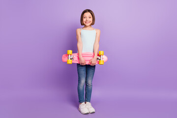 Full length photo of attractive happy nice young little girl hold hands longboard smile isolated on purple color background