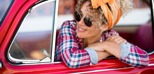 Happy cheerful young adult woman smile and enjoy sitting inside her red trendy car ready to start...