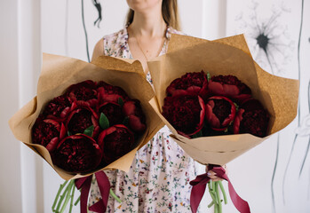 Very nice young woman holding two beautiful mono bouquets of fresh burgundy coloured peonies,...
