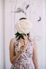 Young woman covering her face with giant mother choice peony flower, vertical photo