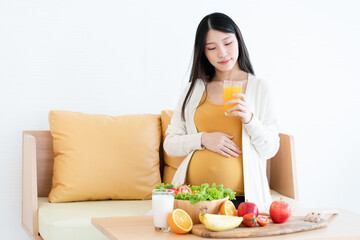 Obraz na płótnie Canvas Asian pregnant woman drinking orange juice and fruits that beneficial to unborn child. Mother and child health care