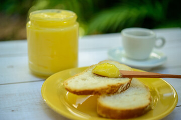 Ghee butter with sliced bread on yellow plate on breakfast table with glass jar of butter and cup in blurred background.