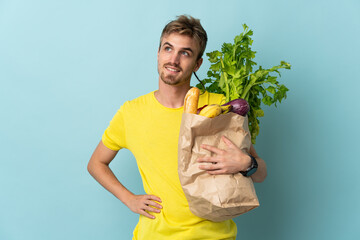 blonde Person taking a bag of takeaway food isolated on blue background posing with arms at hip and...
