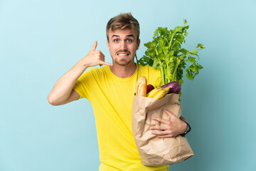 blonde Person taking a bag of takeaway food isolated on blue background making phone gesture. Call...