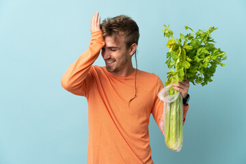 Young blonde man holding a celery isolated on blue background has realized something and intending...