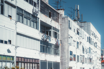 Multiple dwelling houses in a residential district of a European uptown with bright white buildings facades, balconies, dirt and rust, windows, drying laundry, roofs; sunny day, Lisbon, Portugal