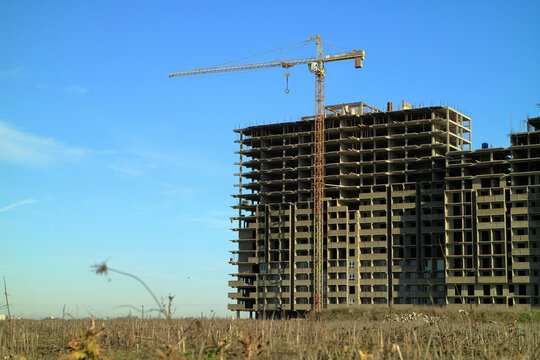 An image of a tower crane against the background of a house under construction.