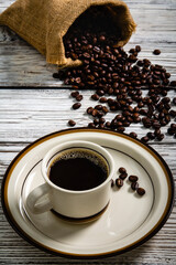 Hot coffee in a coffee cup and coffee beans placed around on an old wooden table in a warm, light atmosphere, on old white wood table background