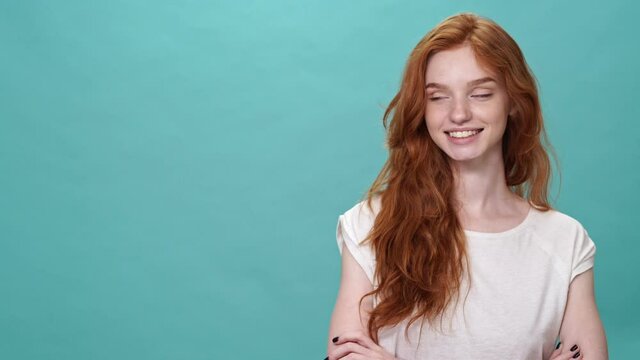 Happy ginger woman in t-shirt posing with crossed arms and pointing away over turquoise background