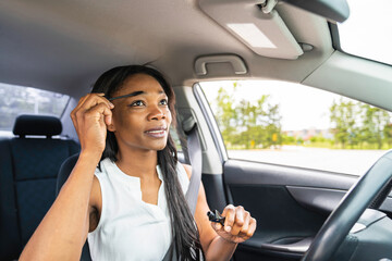 black woman driver seated in her new car holding make up